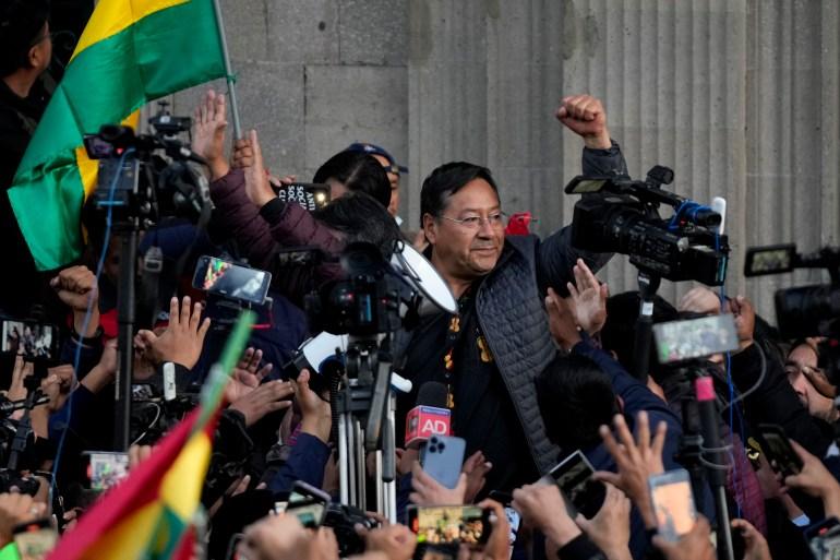 Bolivian President Luis Arce raises a clenched fist surrounded by supporters and media, outside the government palace in La Paz, Bolivia