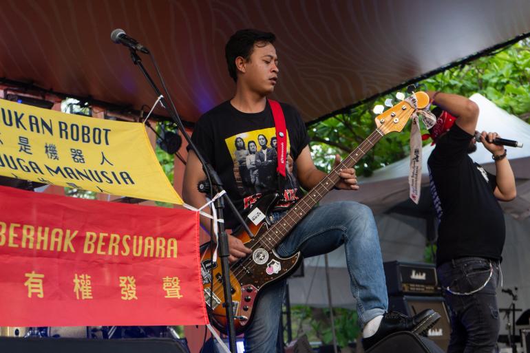 Southern Riot guitarist playing on stage with banners that say 'We are not robots' and 'We are humans too'